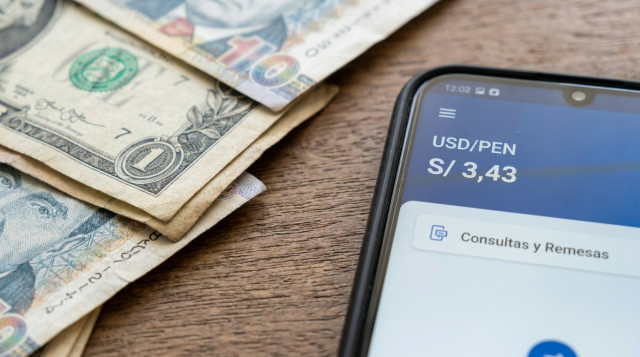 primer plano de billetes de dólares y soles peruanos sobre una superficie neutra, foco en los bordes de los billetes y un smartphone mostrando una aplicación de tipo de cambio con