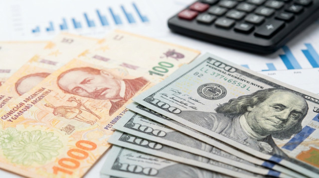 Primer plano de billetes de pesos argentinos y dólares estadounidenses sobre un escritorio de oficina con una calculadora y gráficos financieros de fondo