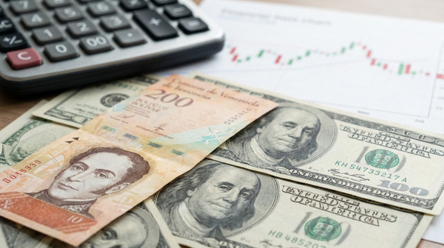 Primer plano de billetes de bolívares venezolanos y dólares estadounidenses sobre una mesa de oficina con una calculadora y un gráfico financiero de fondo