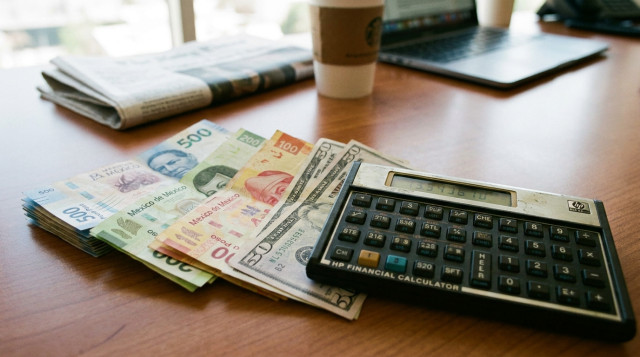 Billetes de pesos mexicanos y dólares estadounidenses dispuestos sobre un escritorio de oficina con una calculadora financiera