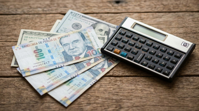 Primer plano de billetes de cien soles peruanos y dólares estadounidenses sobre una mesa de madera con una calculadora financiera